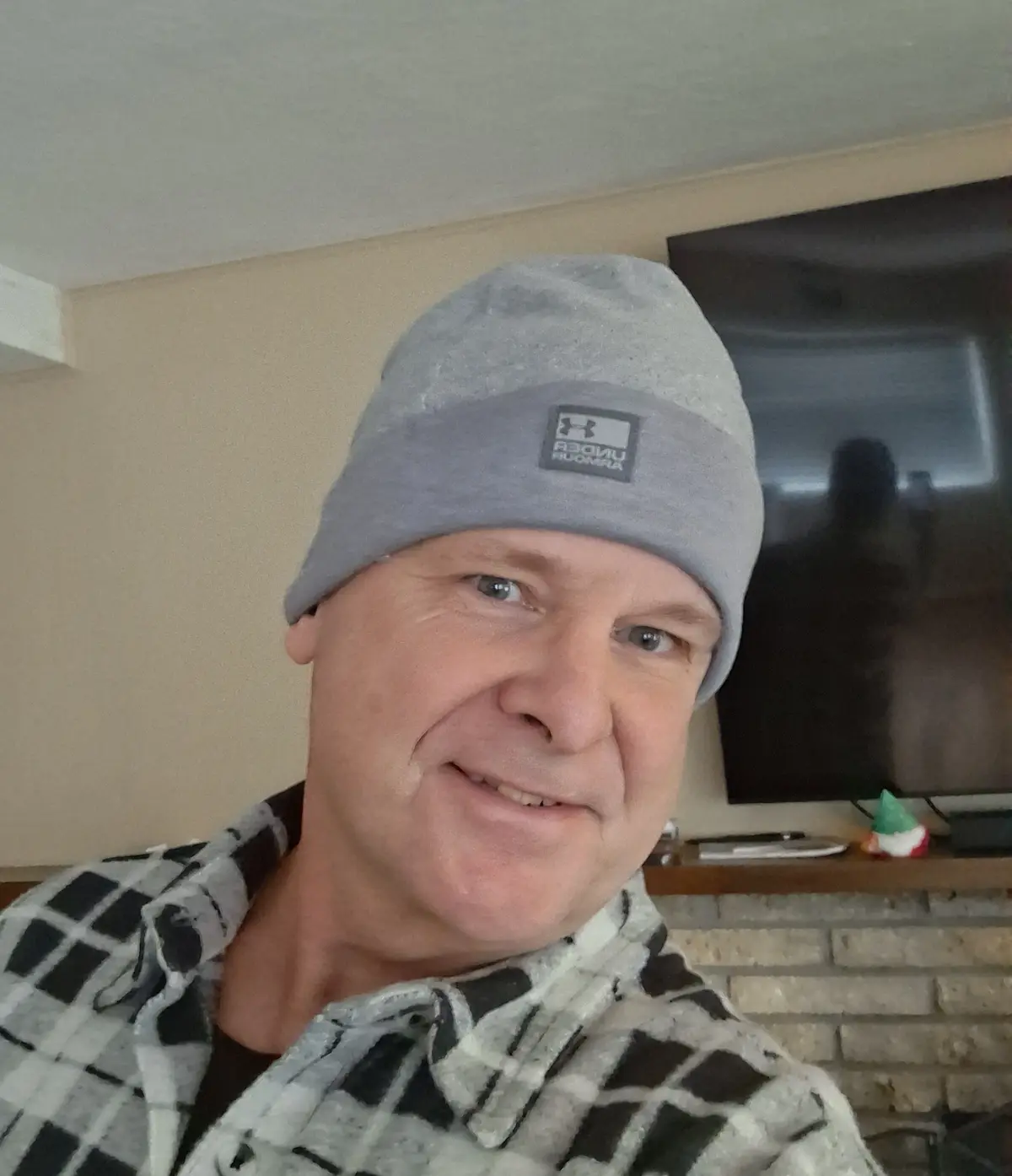 A middle-aged man with blue eyes smiles at the camera while wearing a grey Under Armour beanie and a black-and-white…