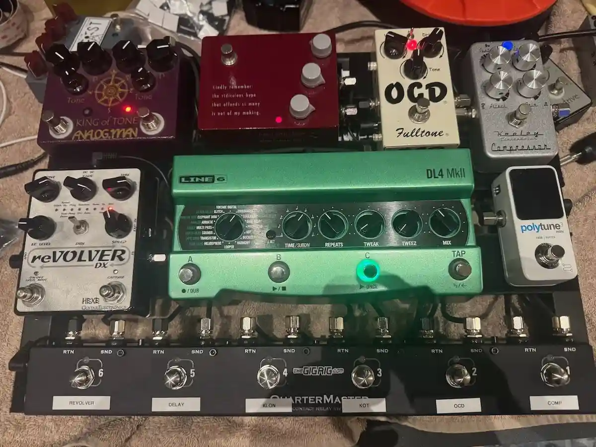 A photo of a densely packed guitar pedalboard featuring multiple effects pedals like the Line 6 DL4 MkII, Fulltone OCD, and…