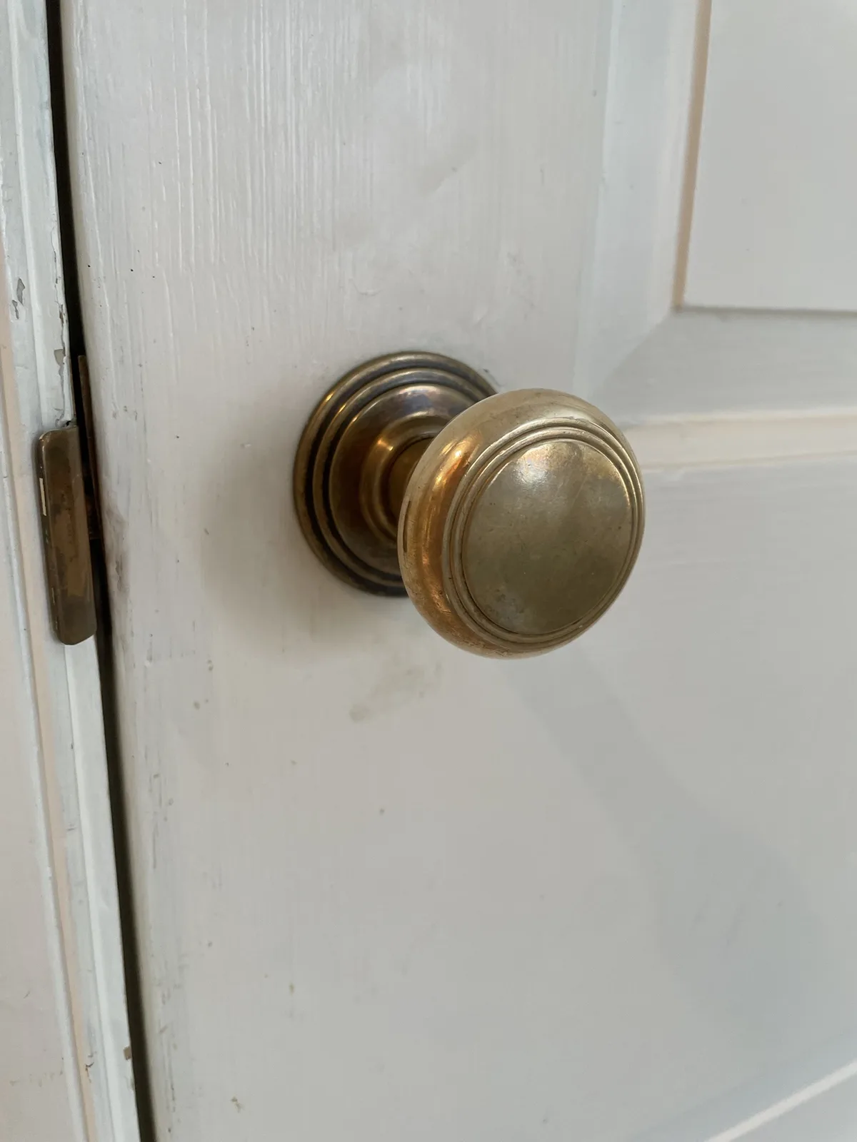 A close-up photo of a brass doorknob on a white wooden door, with visible wear and a slightly ajar door hinge. The overlaid…