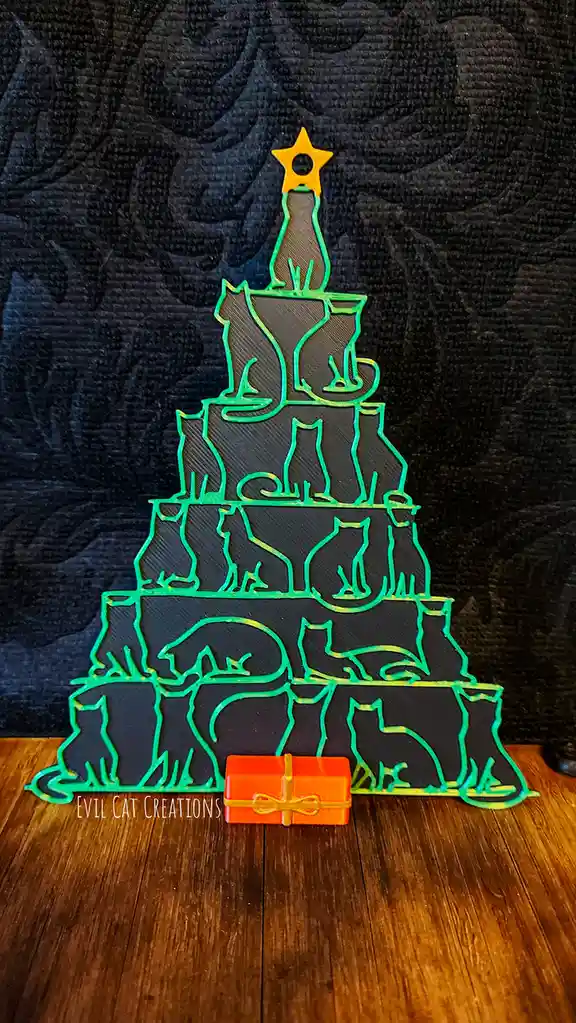 A 3D-printed Christmas tree shaped like a pyramid, decorated with multiple cat silhouettes in green outlines, topped with a…