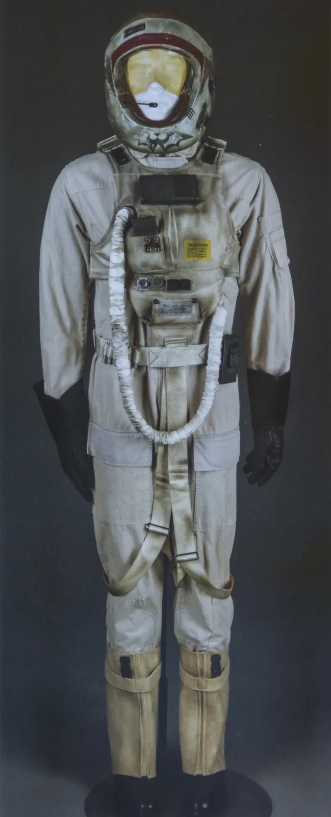 A full-body astronaut suit on a mannequin, featuring a helmet with a yellow-tinted visor and a bat symbol painted on the…