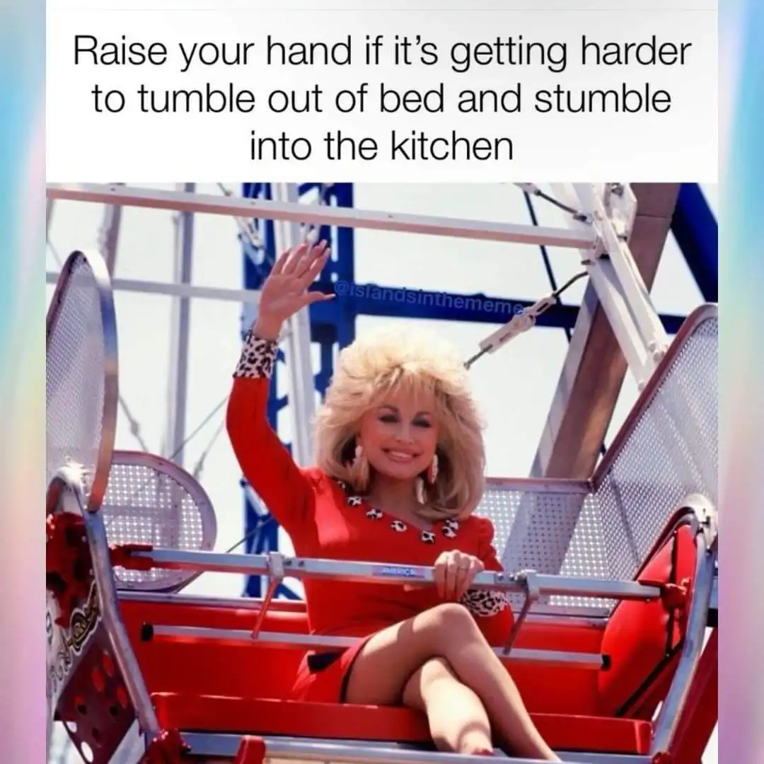 A woman with blonde hair wearing a red dress and leopard-print cuffs sits in a red amusement park ride car, smiling and…