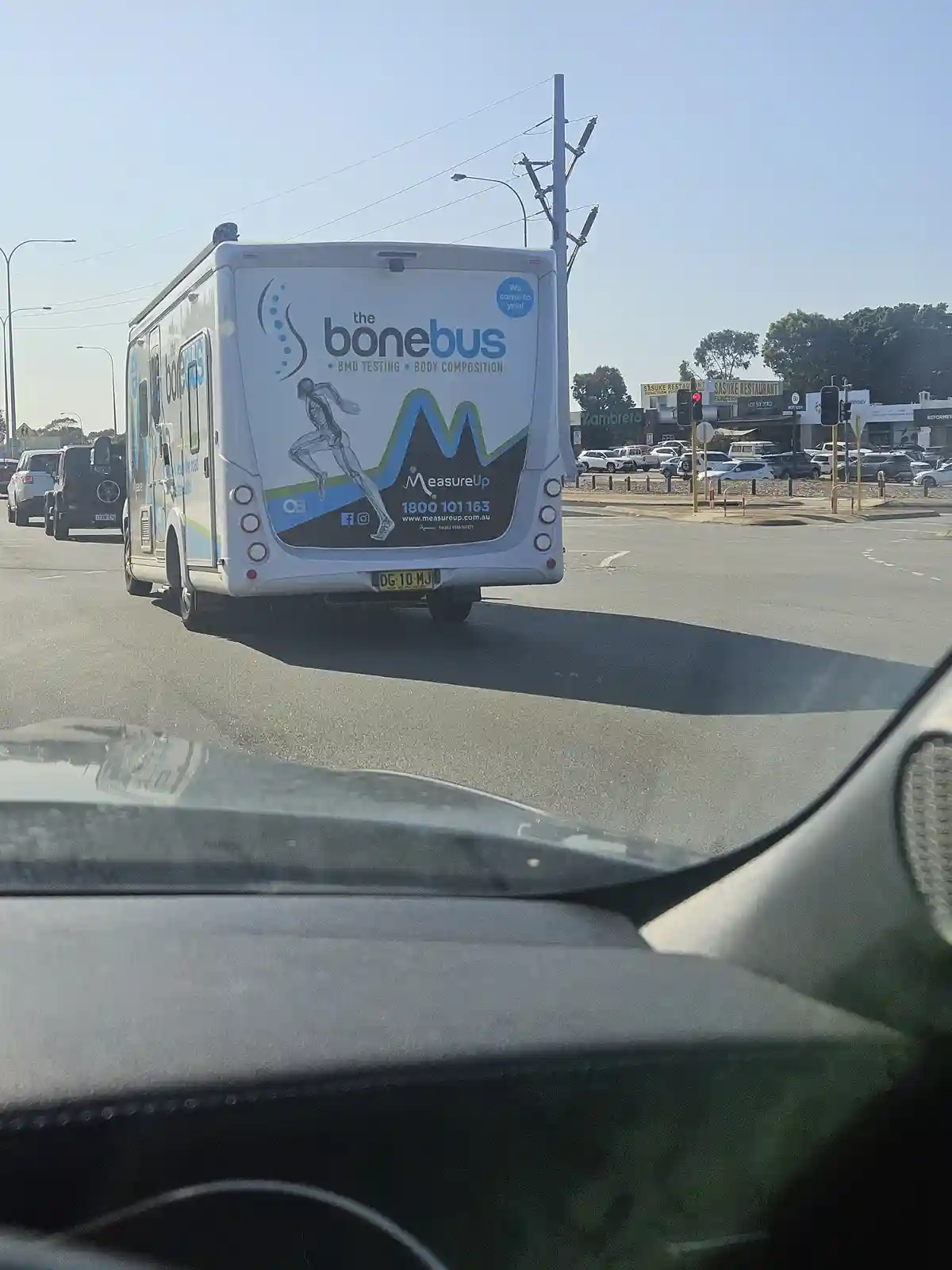 A white mobile medical van, branded 'the bonebus' for BMD testing and body composition, is seen from behind while stopped at…