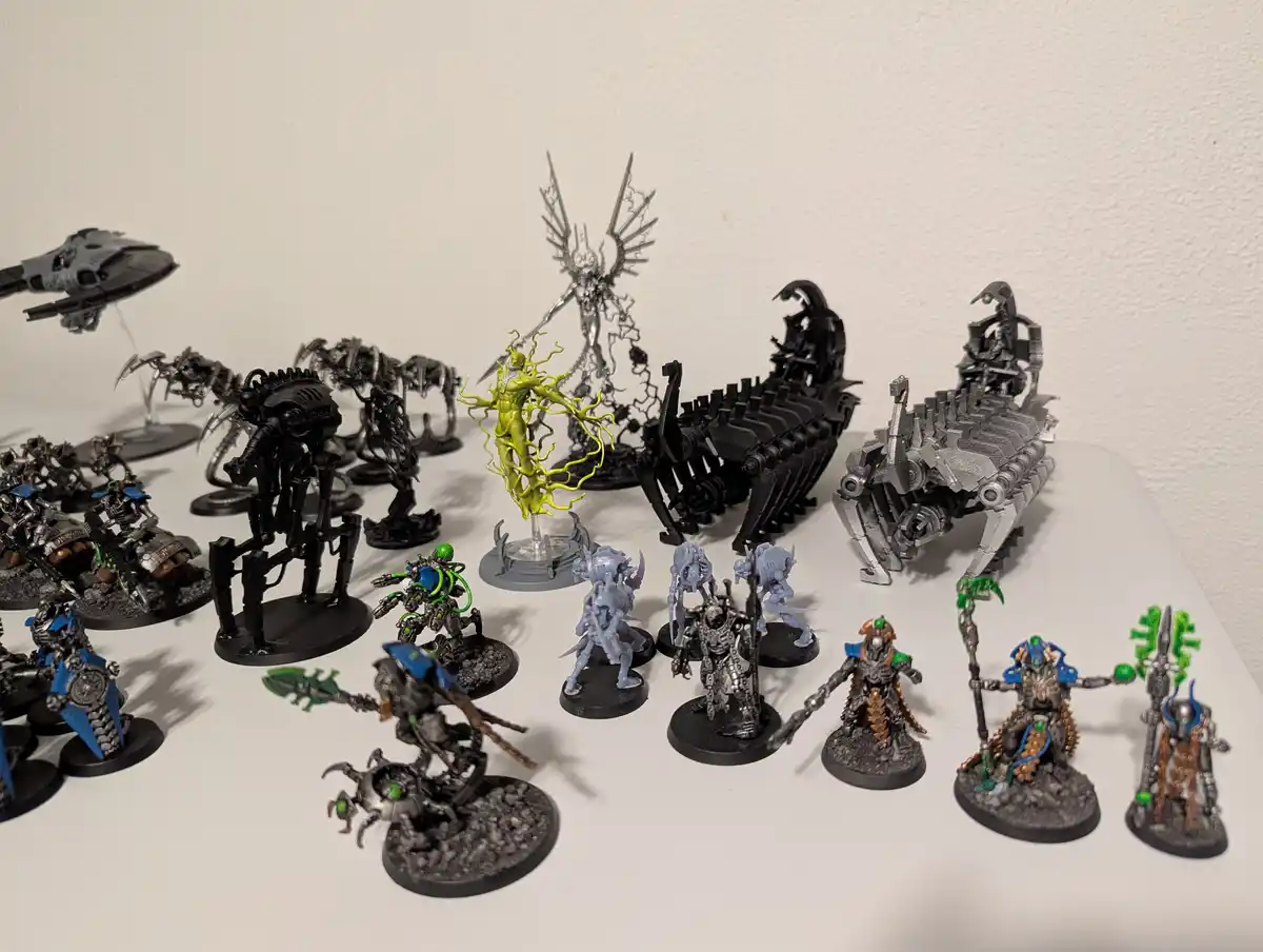 A collection of Warhammer 40k miniatures arranged on a white surface, mostly unpainted or in grey primer, with one…