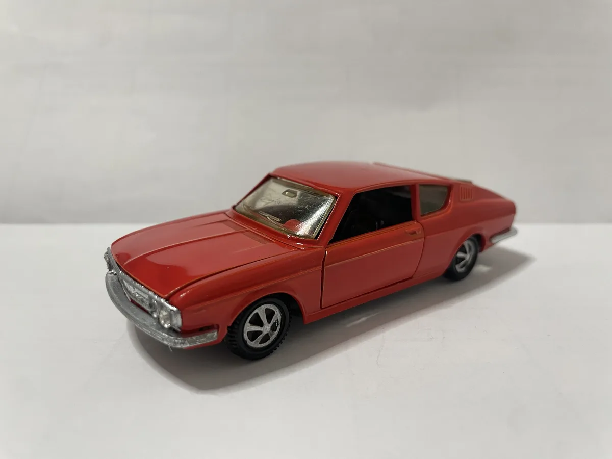 A red toy car model, resembling a classic coupe, is photographed on a plain white surface. The car has silver trim, black…