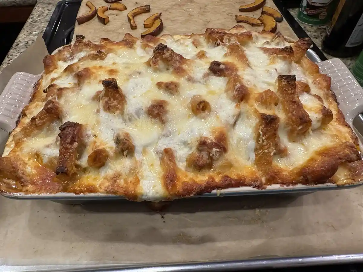 A freshly baked casserole in a white ceramic baking dish sits on parchment paper, its surface covered in melted…