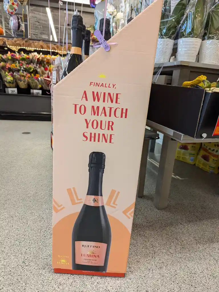 A large, upright cardboard display for Ruffino Lumina Prosecco sparkling wine stands in a grocery store aisle, featuring an…