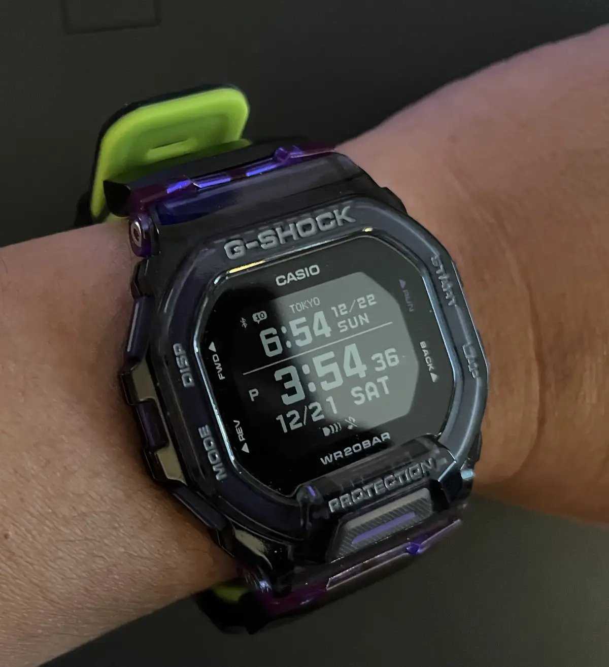 A close-up of a Casio G-Shock watch on a person's wrist, displaying two time zones: the top shows 6:54 on Sunday, December…