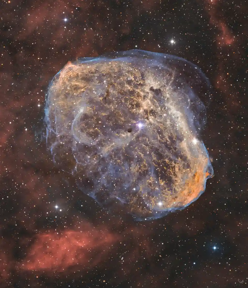 a cosmic image of a supernova remnant with a distinct skull-like shape, featuring a dark eye socket and a glowing nasal…
