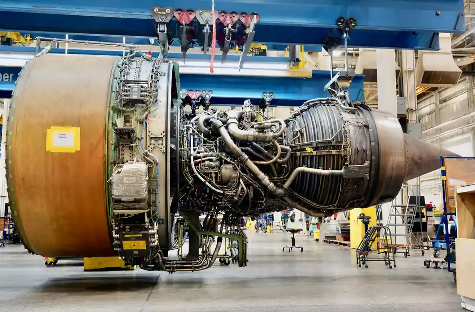 A large, complex jet engine, identified by a yellow label as 'UNITED PW4090', is suspended in a factory or hangar, revealing…