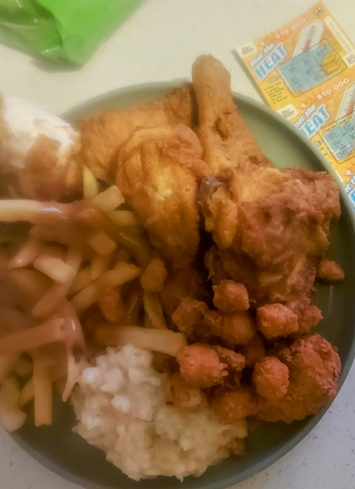 A plate of fried chicken, french fries, and mashed potatoes sits next to a lottery ticket labeled 'Beat the Heat' with a…