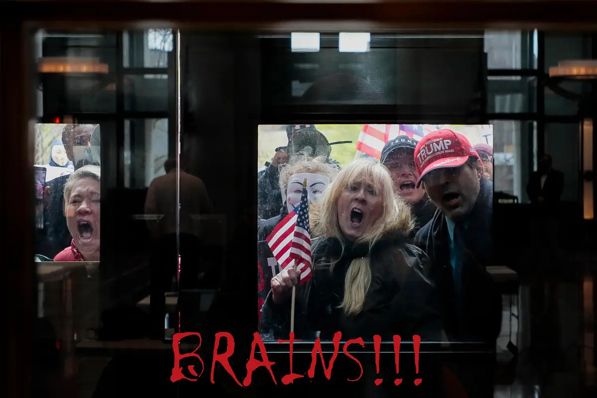 A photo shows a group of people, some wearing Trump hats and holding American flags, shouting through a glass window. One…