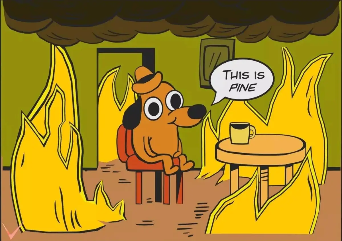 A cartoon dog wearing a hat sits calmly in a room engulfed in flames and smoke, smiling while saying 'THIS IS FINE' in a…