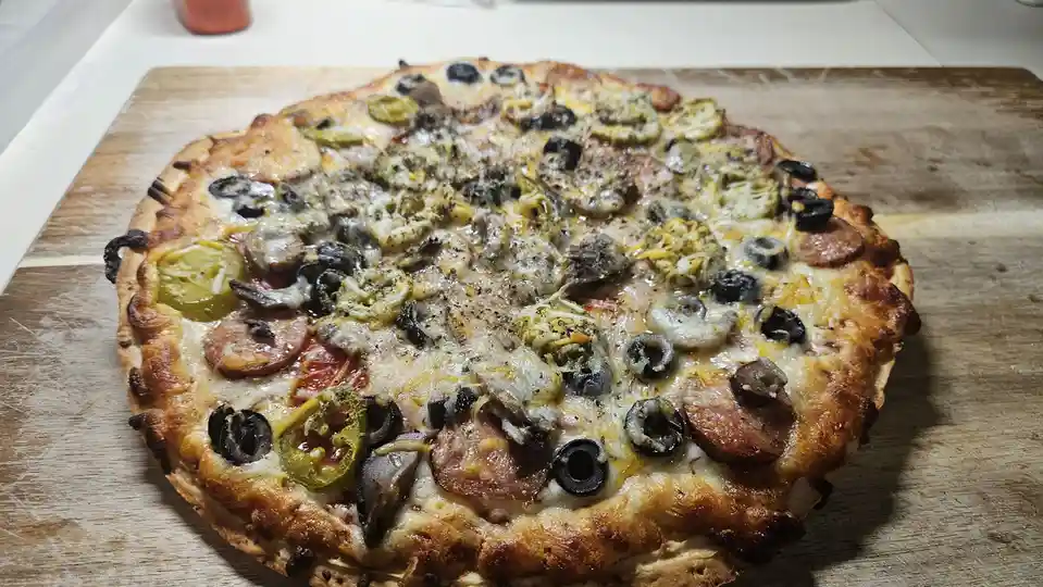 A freshly baked pizza with a golden-brown crust sits on a wooden cutting board, covered in a chaotic mix of toppings…
