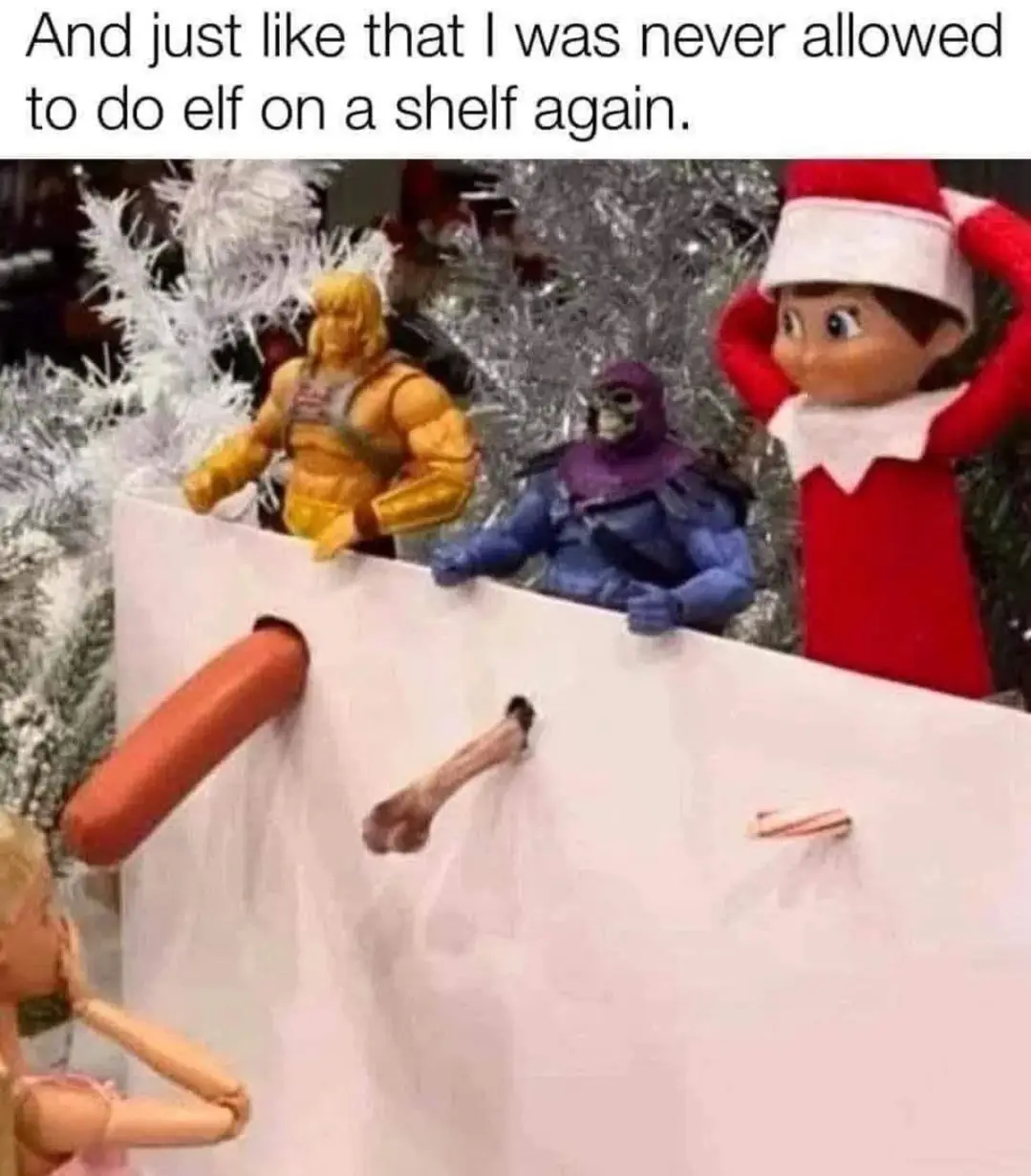 A toy elf in a red outfit with a white hat stands behind a white cardboard barrier, looking shocked with hands on head…