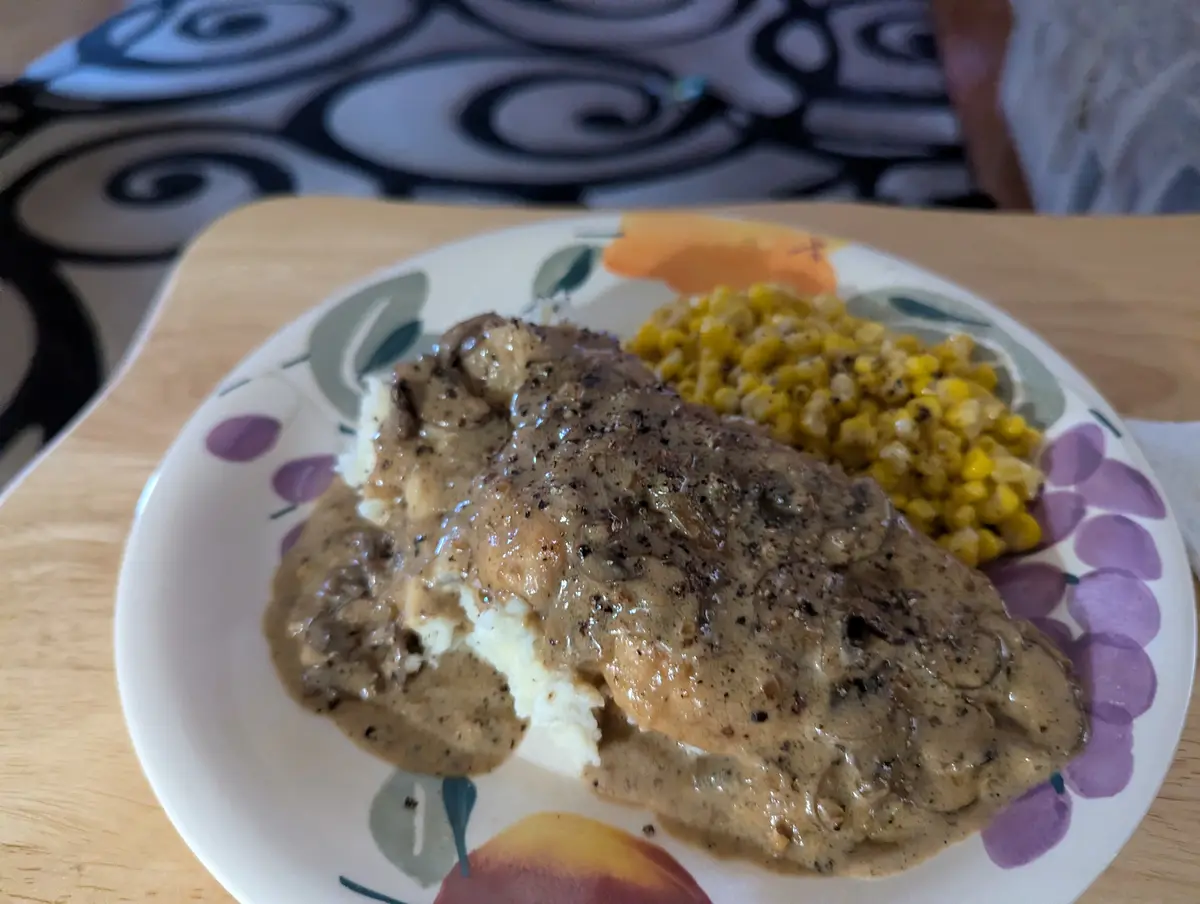 A close-up photo shows a plate of food featuring a meat dish covered in gravy over mashed potatoes, alongside a serving of…