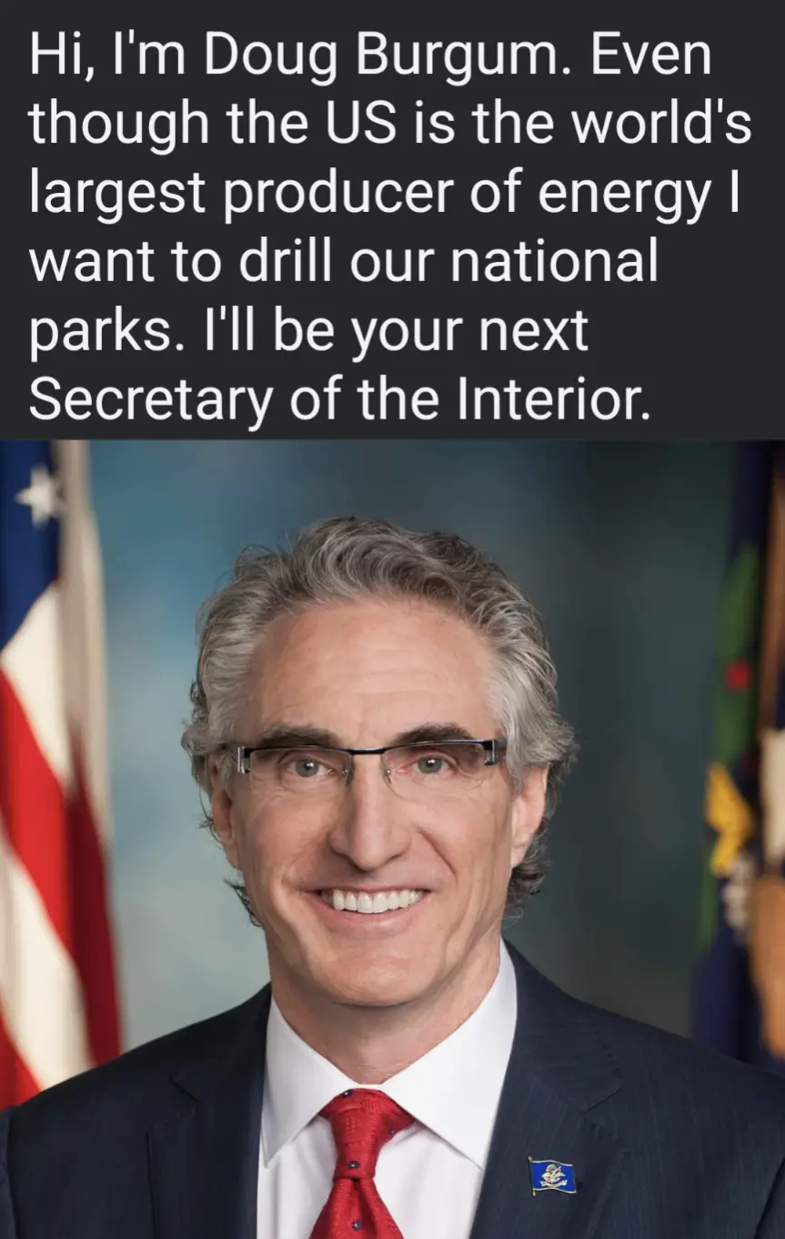 A formal portrait of Doug Burgum, a man with gray hair and glasses wearing a dark suit, white shirt, and red tie, smiling in…
