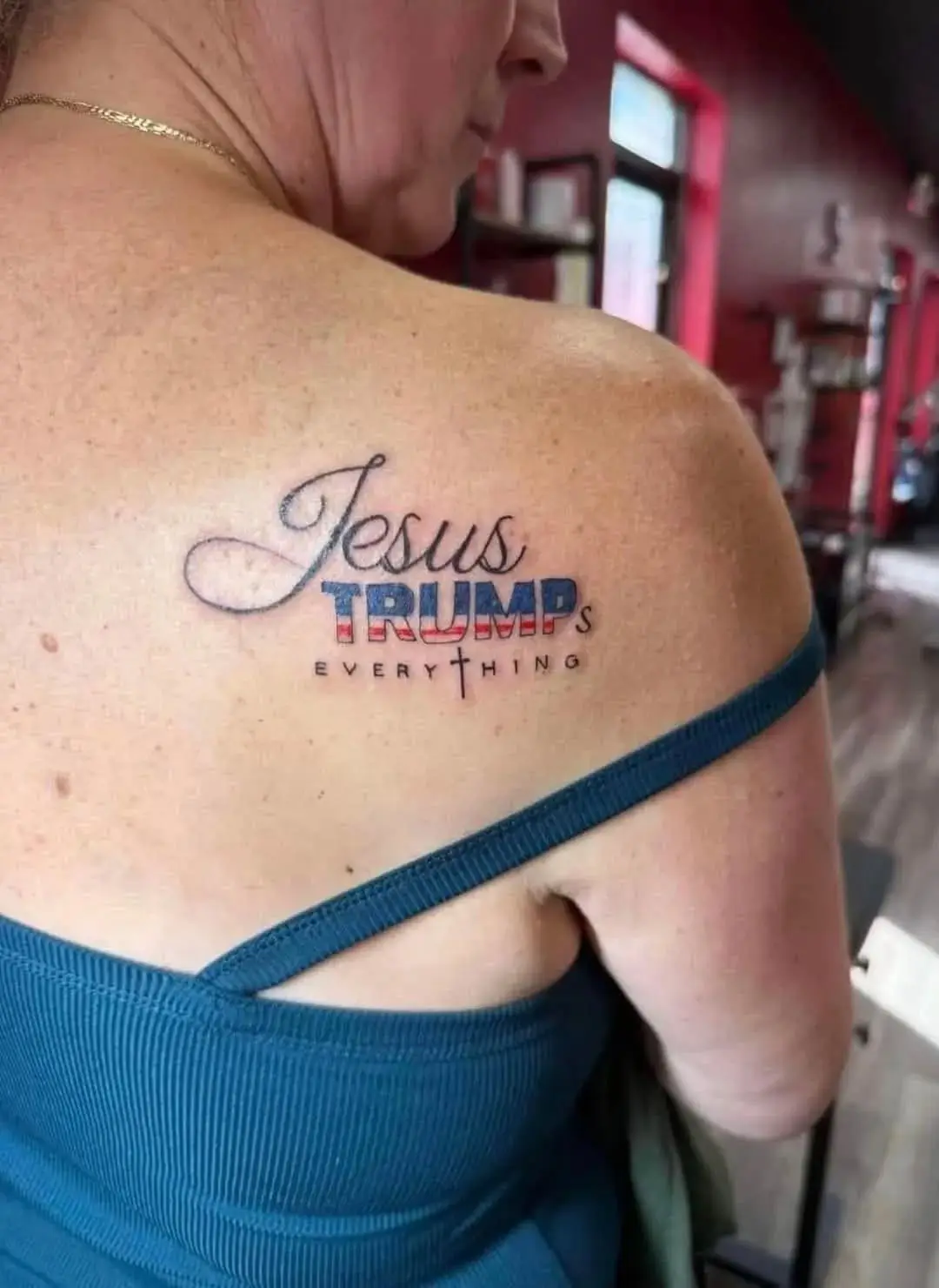 A close-up photo shows the upper back and shoulder of a person wearing a blue top, revealing a tattoo that reads 'Jesus…