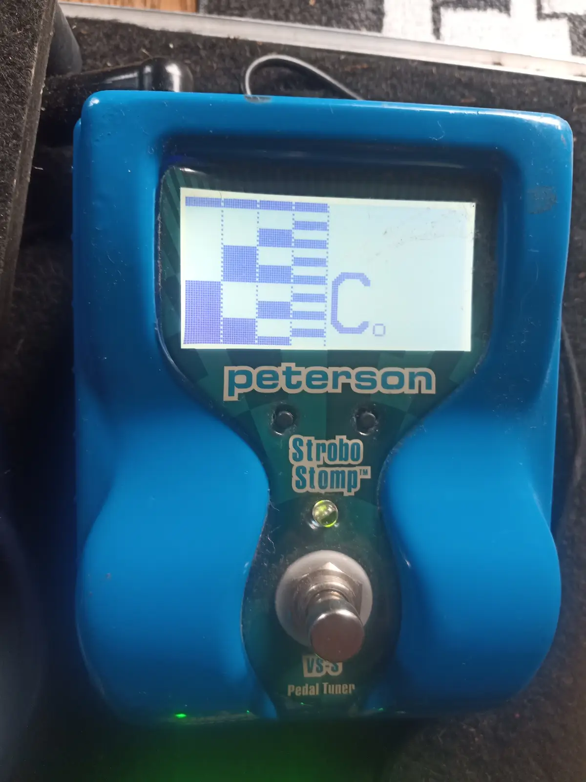 A blue Peterson Strobo Stomp VS-3 pedal tuner displays a tuning screen showing the note 'C.' with a stroboscopic pattern…