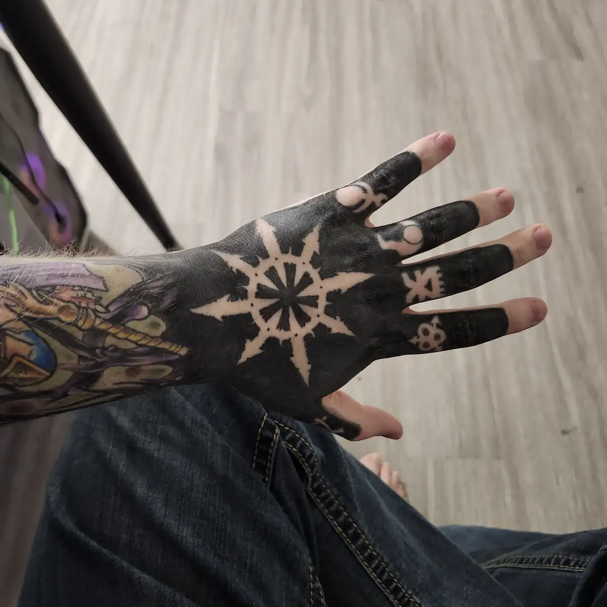 A person's hand is shown with a large, intricate white snowflake tattoo on the palm, set against a black background covering…