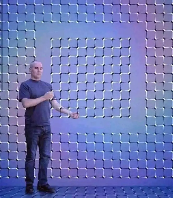 A man in a dark t-shirt and jeans stands in front of a large, glowing grid pattern that forms the shape of the letter 'I' on…