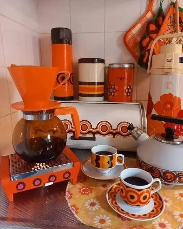 A vintage 1970s kitchen scene featuring orange and brown patterned coffee equipment, including a pour-over dripper, matching…