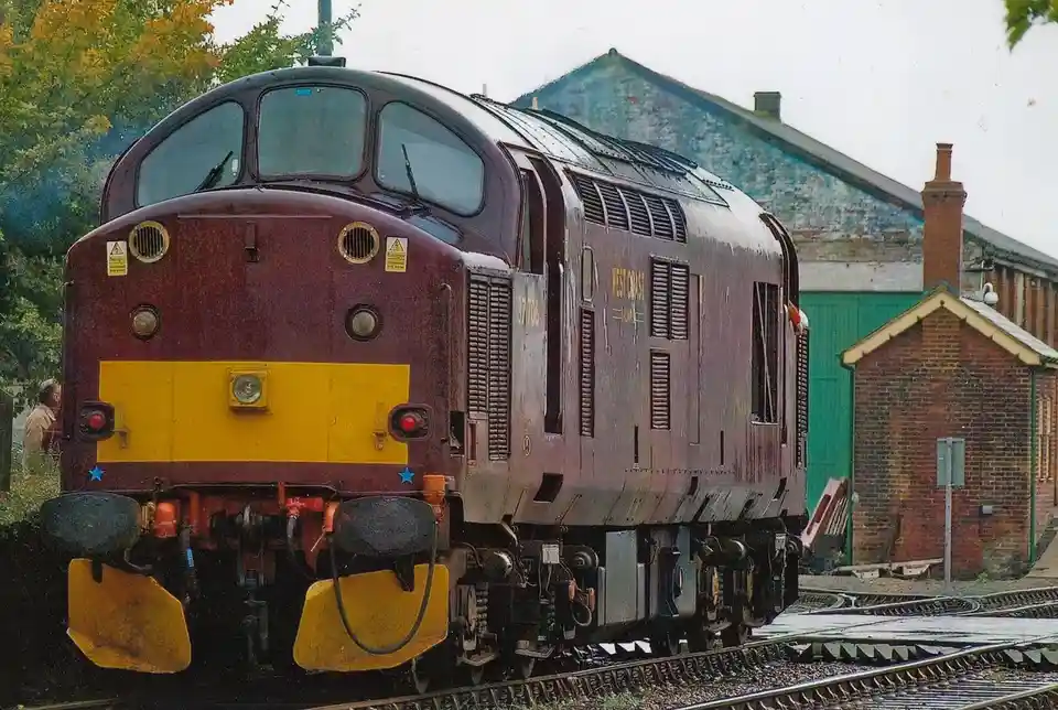A maroon and yellow British Rail Class 57 diesel locomotive, number 57 706, is pictured on railway tracks with brick and…