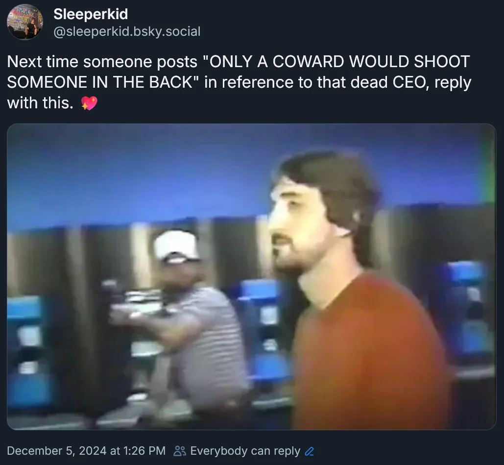 A low-resolution, blurry image shows a man in a red shirt standing in profile, looking toward the right, while another man…