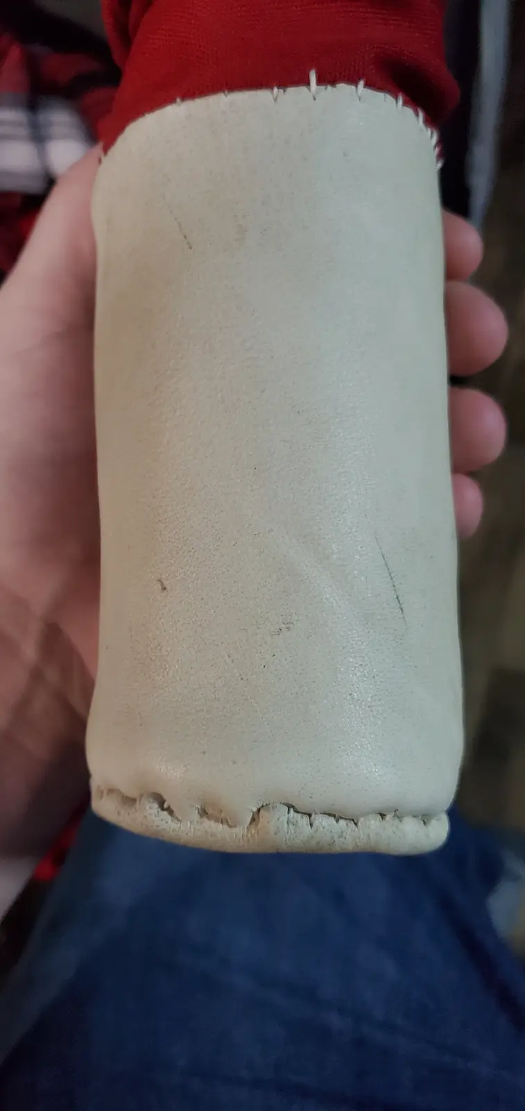 A close-up photo shows a person's hand holding a worn, beige, cylindrical shoe sole with visible stitching and frayed edges…