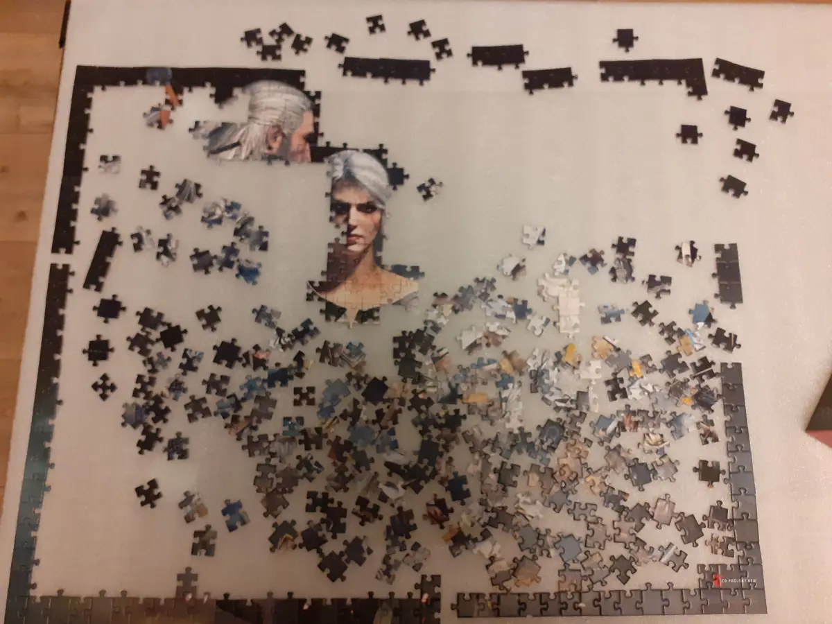 A partially completed jigsaw puzzle of Geralt and Ciri from The Witcher, with most pieces scattered around the board…