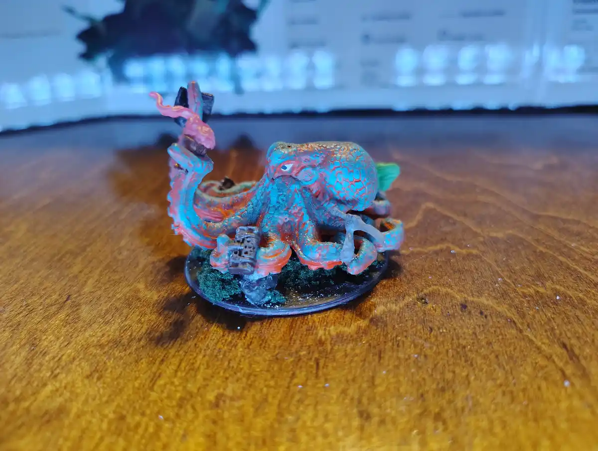 A painted miniature octopus figurine sits on a wooden surface, holding a small beer mug in one tentacle while another…